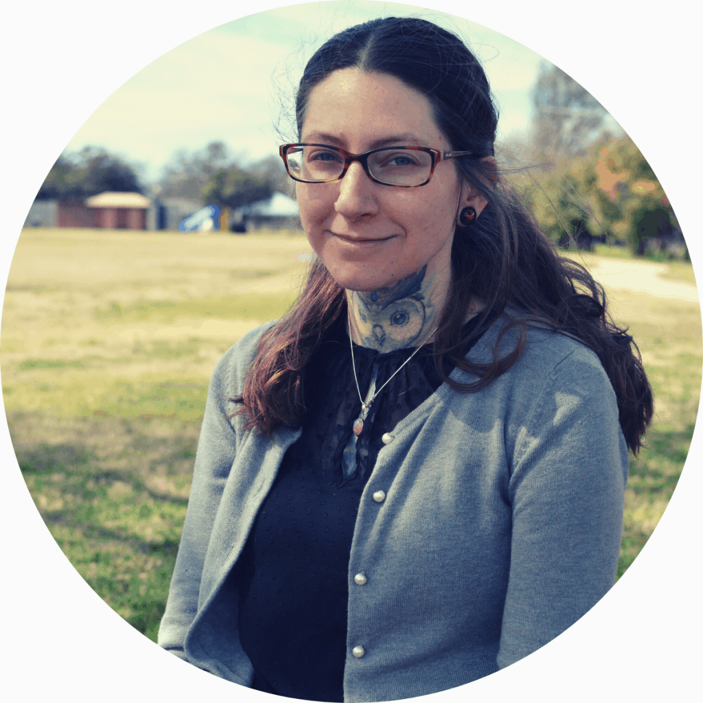 Woman with brown hair, glasses and owl neck tattoo sitting outside in the park