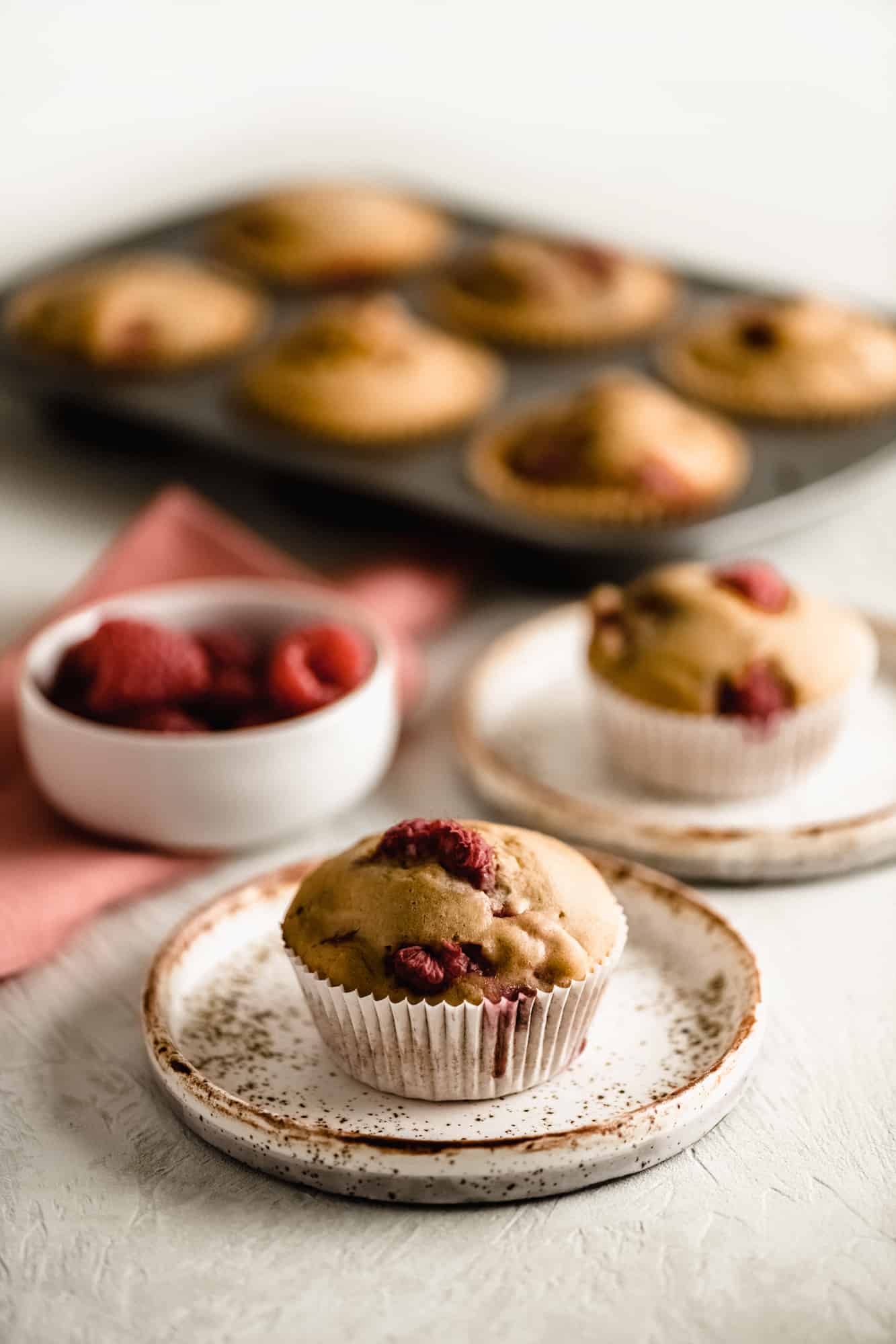 Tray of raspberry muffins, 2 small plates each with a raspberry muffin and a tiny bowl of fresh raspberries