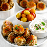 Pile of sausage balls with golden crispy cheese next to ranch dip
