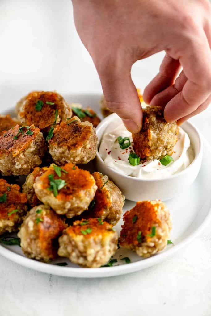 Pile of sausage balls with golden crispy cheese being dipped into ranch dip
