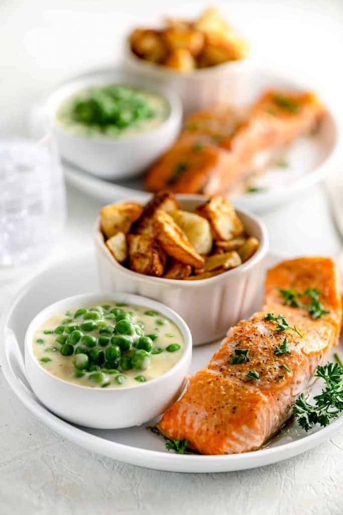 cup of creamed peas beside a cup of roasted potatoes and fillet of salmon
