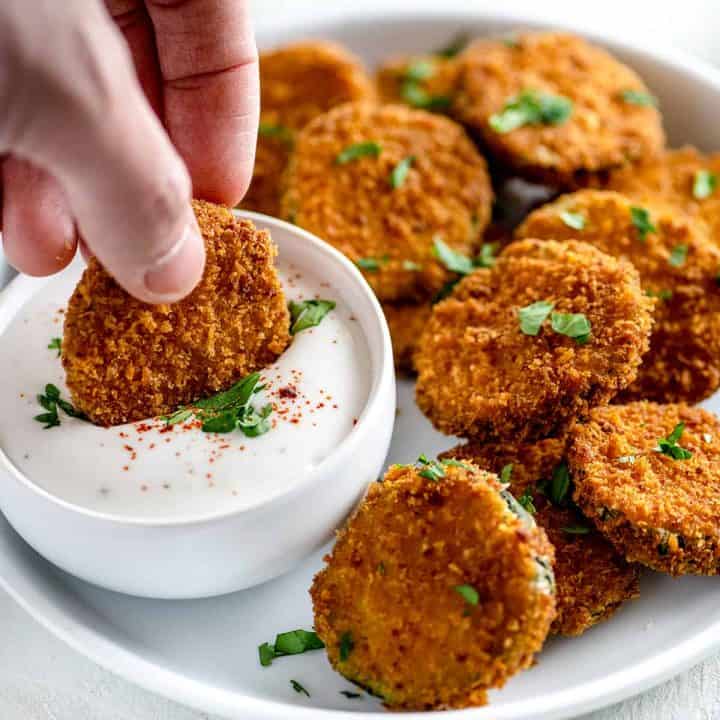 White plate full of crispy fried cucumbers with one being dipped in ranch