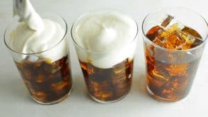 three glasses of iced coffee with cream cheese foam being spooned on top