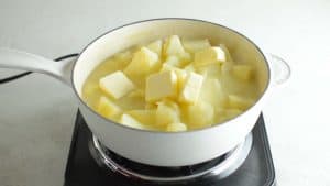 chunks of butter in a white pan of stewed potatoes