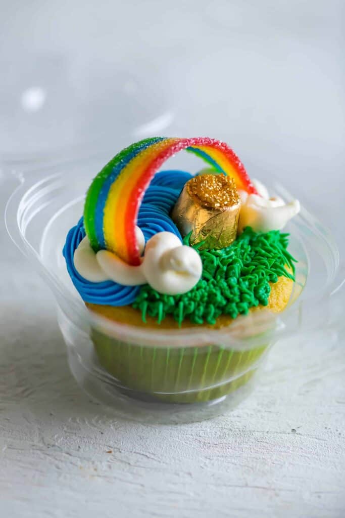 St Patricks day cupcake decorated with green grass, blue sky, white clouds with a rainbow and pot of gold