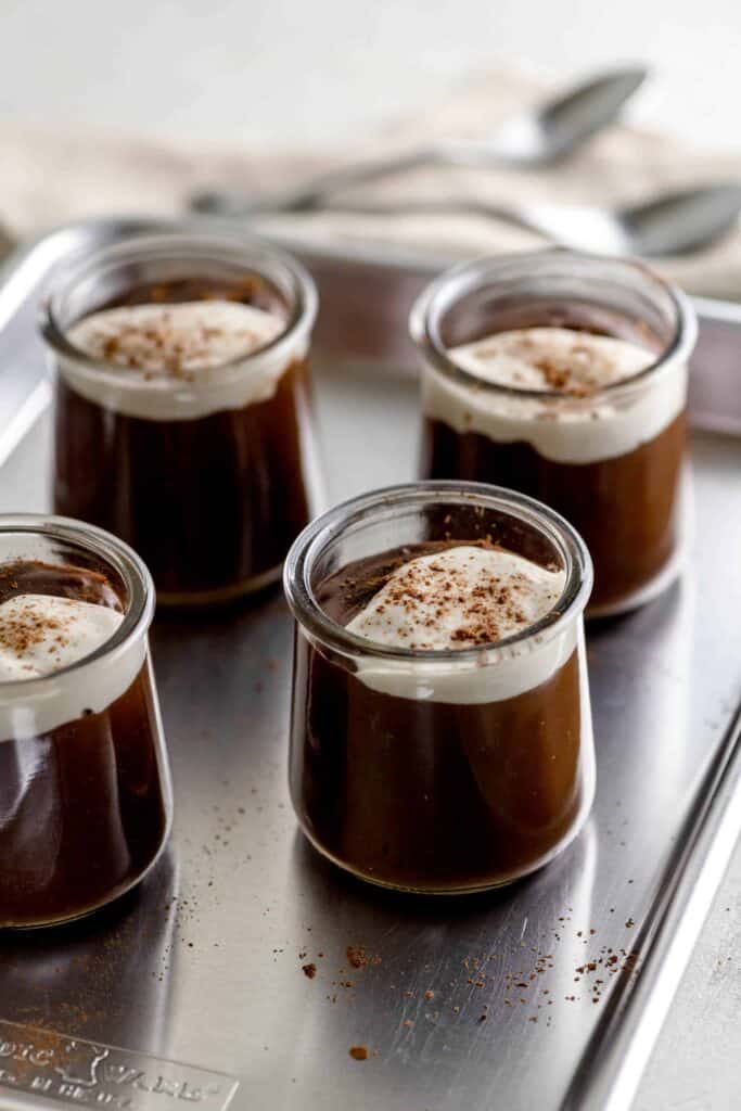 4 glass jars filled with chocolate pudding on a baking sheet with spoons and a clothe napkin
