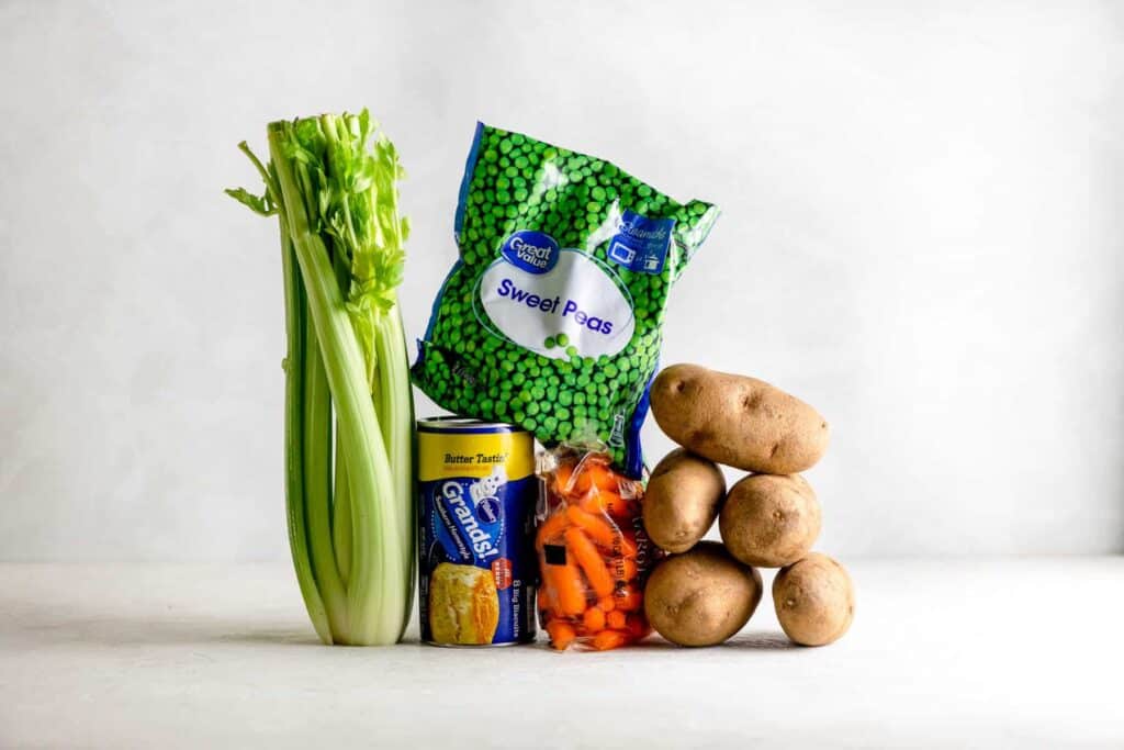 Celery, carrots, potatoes, bag of frozen peas with a can of biscuits on a gray table