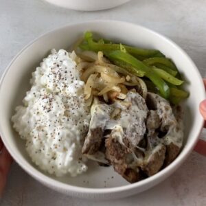 high-protein philly cheesesteak cottage cheese bowl with steak bites, melted provolone, peppers, onions, and cottage cheese